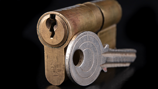 brass locking cylinder and silver key on black backdrop